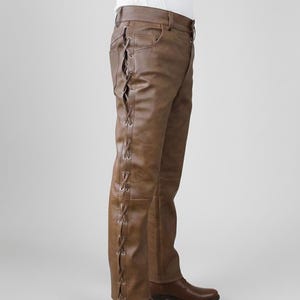 May include: Brown leather trousers featuring a side lace-up detail with metal eyelets running down the outer leg. The trousers have a structured waistband with belt loops and are paired with matching brown leather boots that reach the ankle.