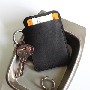 May include: A black leather wallet with a key ring and a key attached. The wallet is sitting in a silver metal dish.