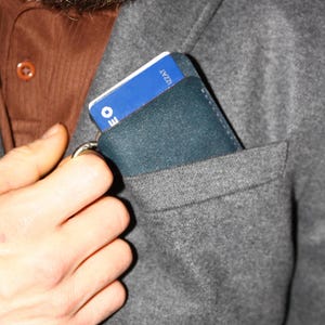 May include: A dark blue leather wallet with a blue and white card inside. The wallet is in a gray pocket.