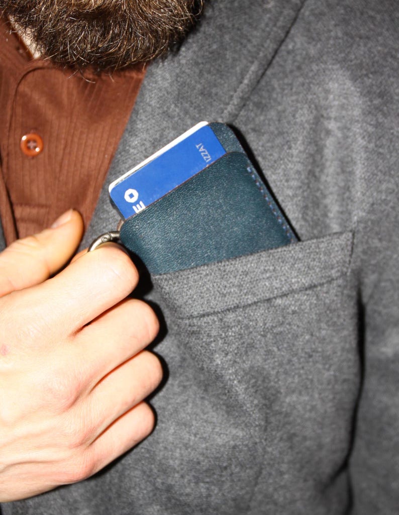 May include: A dark blue leather wallet with a blue and white card inside. The wallet is in a gray pocket.