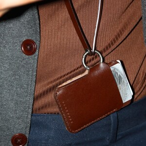 May include: A brown leather card holder with a silver clasp and the text "ULAGGOODS" on the front. The card holder is attached to a brown and white lanyard.