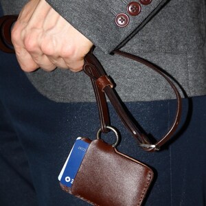 May include: A brown leather ID badge holder with a blue card inside. The holder is attached to a brown leather strap with a metal ring.