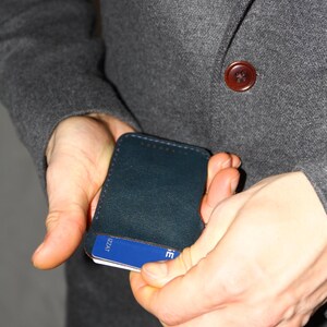 May include: A person is holding a dark blue leather card holder with a blue card inside. The card has the text "VISA" printed on it.