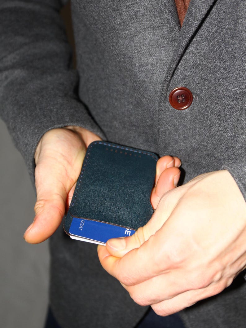 May include: A person is holding a dark blue leather card holder with a blue card inside. The card has the text "VISA" printed on it.