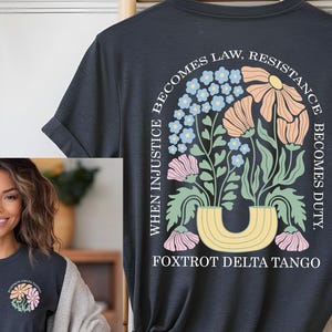 May include: Dark gray t-shirt with a floral design on the back, featuring the text "WHEN INJUSTICE BECOMES LAW, RESISTANCE BECOMES DUTY." The design includes flowers in shades of pink, peach, and blue. The text "FOXTROT DELTA TANGO" is below the floral arrangement.