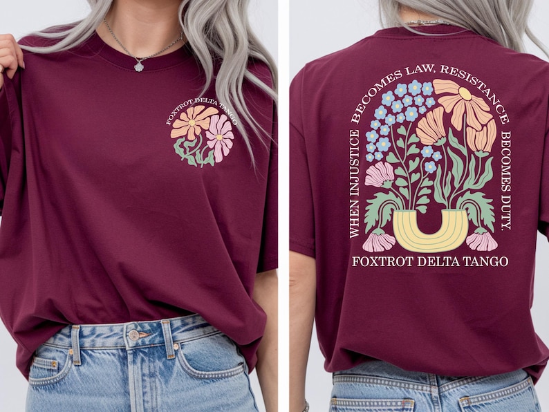 May include: Burgundy t-shirt with a floral design on the front and back. The front features a flower graphic with the text "Foxtrot Delta Tango." The back displays a floral arrangement with the text "When injustice becomes law, resistance becomes duty."
