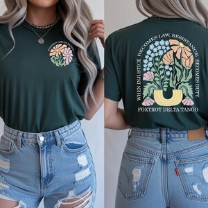 May include: Dark green t-shirt with a floral design on the front and back. The front features a circular design with flowers and the text "FOXTROT DELTA TANGO." The back displays a floral arrangement and the text "WHEN INJUSTICE BECOMES LAW, RESISTANCE BECOMES DUTY."