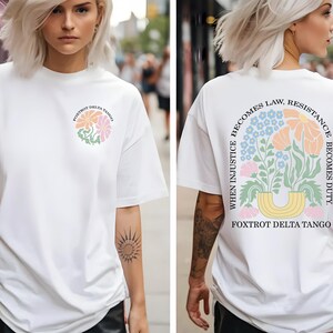 May include: White t-shirt with a floral design and the text "Foxtrot Delta Tango" on the front. The back of the shirt features a floral arrangement and the quote "When injustice becomes law, resistance becomes duty."