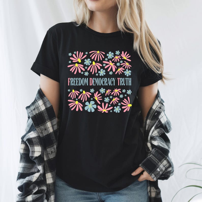 May include: Black t-shirt with a floral design in pink, blue, and yellow. The text "FREEDOM DEMOCRACY TRUTH" is printed below the flowers. The shirt is a crew neck and short-sleeved.