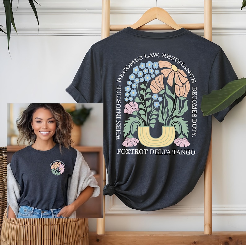 May include: Dark gray t-shirt with a floral design on the back, featuring the text "WHEN INJUSTICE BECOMES LAW, RESISTANCE BECOMES DUTY." The design includes flowers in shades of pink, peach, and blue. The text "FOXTROT DELTA TANGO" is below the floral arrangement.