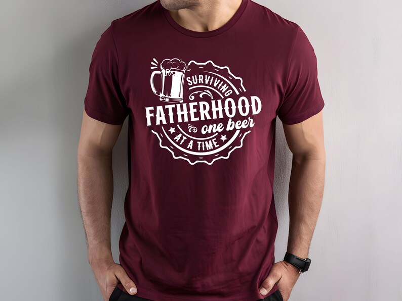 May include: Burgundy t-shirt with a white graphic of a beer mug and the text "Surviving Fatherhood one beer at a time".