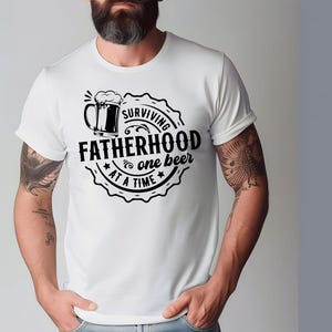 May include: White t-shirt with a black graphic design of a beer mug and the text "Surviving Fatherhood one beer at a time".