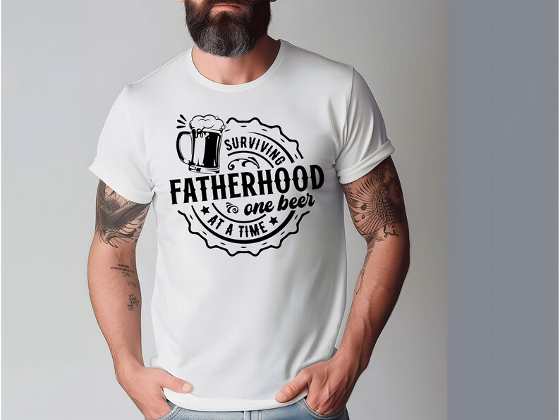 May include: White t-shirt with a black graphic design of a beer mug and the text "Surviving Fatherhood one beer at a time".