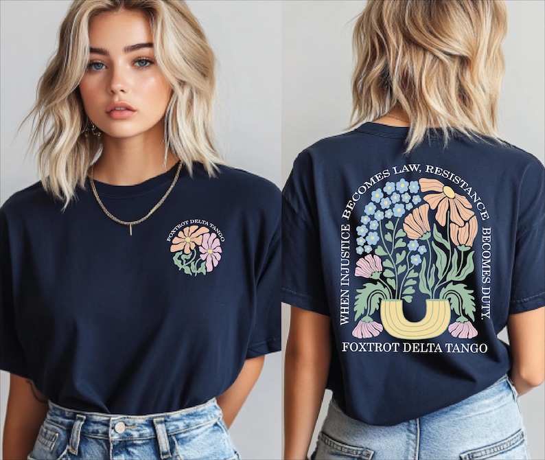 May include: Navy blue t-shirt with a floral design on the front and back. The front features a small floral graphic, while the back displays a larger arrangement with text that reads "When Injustice Becomes Law, Resistance Becomes Duty." The text "Foxtrot Delta Tango" is also present.