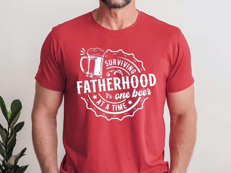May include: Red t-shirt with a white graphic design of a beer mug and the text "Surviving Fatherhood one beer at a time".