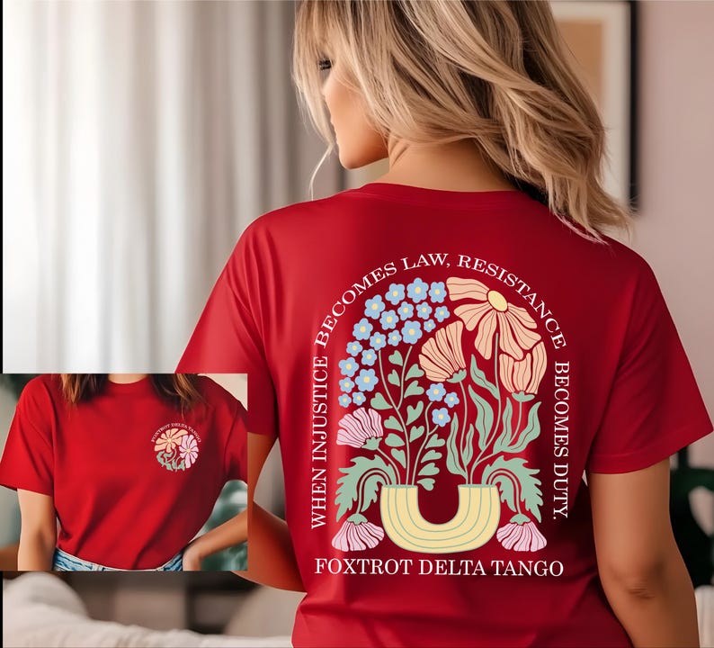 May include: A red t-shirt with a floral design on the back, featuring a variety of flowers in pastel colors and the text "WHEN INJUSTICE BECOMES LAW, RESISTANCE BECOMES DUTY." The shirt also has a smaller floral design on the front.