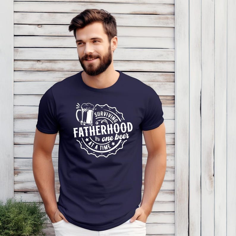 May include: A navy blue t-shirt with a white graphic of a beer mug and the text "Surviving Fatherhood one beer at a time".