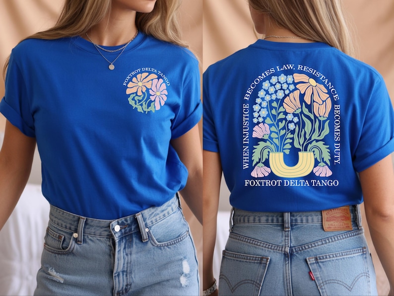 May include: Royal blue t-shirt with a floral design on the front and back. The front features a circular floral design with the text "Foxtrot Delta Tango". The back has a floral arch with the text "When injustice becomes law, resistance becomes duty."