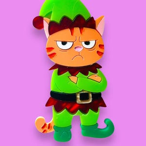 May include: A grumpy orange cat wearing a green elf costume with a red collar and hat. The cat has a black belt with a gold buckle and is standing on a purple background. The cat's arms are crossed.