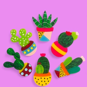 May include: A set of seven colorful, hand-painted wooden cactus and succulent plants in pots. The plants are all different shapes and sizes, and the pots are decorated with geometric patterns and polka dots.