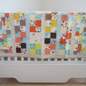 May include: A white crib with a patchwork quilt in shades of brown, orange, yellow, and blue. The quilt is made of squares with different patterns and designs.