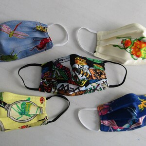 May include: Five different fabric face masks with various insect and nature-themed prints. The masks are all folded and have elastic ear loops. The prints include a dragonfly, a beetle, a bee, a caterpillar, and a magnifying glass with a dragonfly inside.