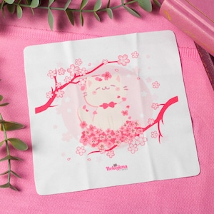 Könnte beinhalten: Ein weißes Mikrofaser-Reinigungstuch mit einer rosa und weißen Illustration einer Katze, die in einem Kirschblütenbaum sitzt. Der Text "Thelojima" ist in der Mitte unten auf dem Tuch gedruckt.