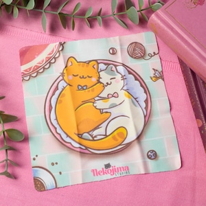 Puede incluir: Una ilustración linda de dos gatos acurrucados en un tazón rosa y azul. El gato naranja lleva una corbata de moño y el gato blanco lleva un moño rosa. La ilustración está sobre un fondo blanco con un patrón de azulejos azules y verdes.
