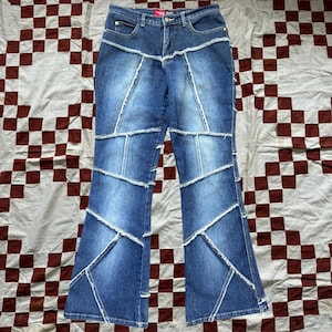 May include: Blue denim jeans with a patchwork design. The jeans have a flared leg and are made of multiple pieces of denim sewn together.