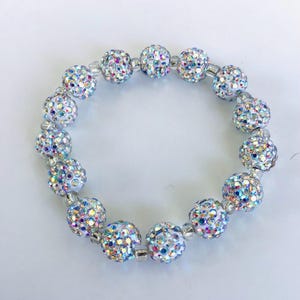 May include: A sparkling bracelet featuring iridescent, crystal-covered beads. The round beads are strung together with small, clear beads and silver-toned connectors. The bracelet has a bright, eye-catching appearance.