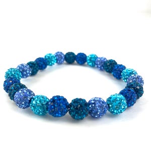 May include: A blue and turquoise beaded bracelet with round, sparkly beads. The beads are arranged in a gradient pattern, starting with dark blue and transitioning to turquoise.