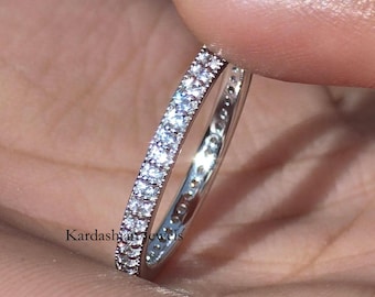 Puede incluir: Un anillo plateado con dos filas de pequeñas piedras preciosas claras. El anillo se sostiene entre los dedos, mostrando sus detalles brillantes. El anillo es una joya.