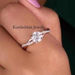May include: A diamond engagement ring with a round center stone and a split shank band. The ring is set with small accent diamonds. The text "Kardashian Jewels" is visible.