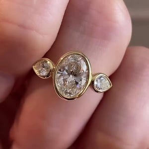 May include: A gold ring with three oval-shaped diamonds. The center diamond is larger than the two side diamonds.