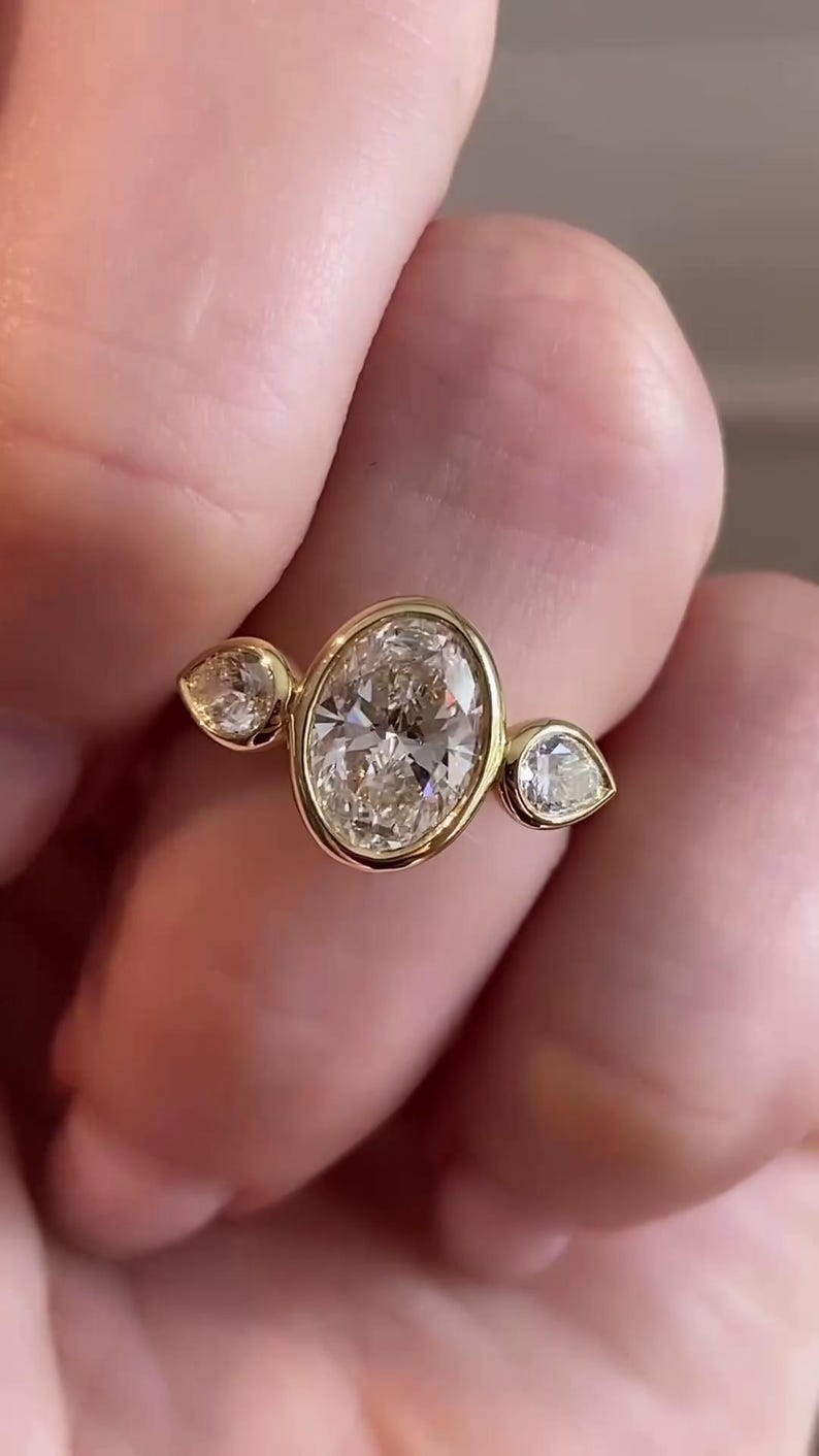 May include: A gold ring with three oval-shaped diamonds. The center diamond is larger than the two side diamonds.