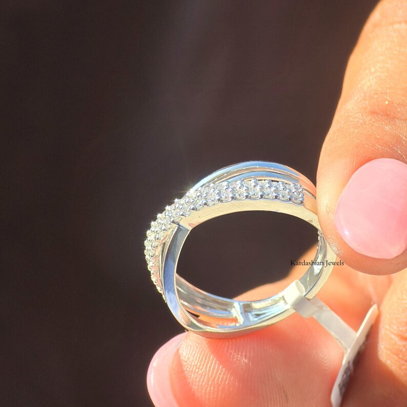 May include: A silver ring with a curved design, featuring a row of small, sparkling stones. The ring has a modern, elegant style. The text "Kardashian Jewels" is visible on the ring.