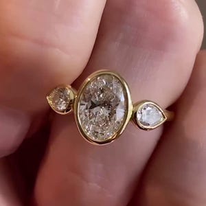 May include: A gold ring with a large oval-shaped diamond and two smaller pear-shaped diamonds on either side.