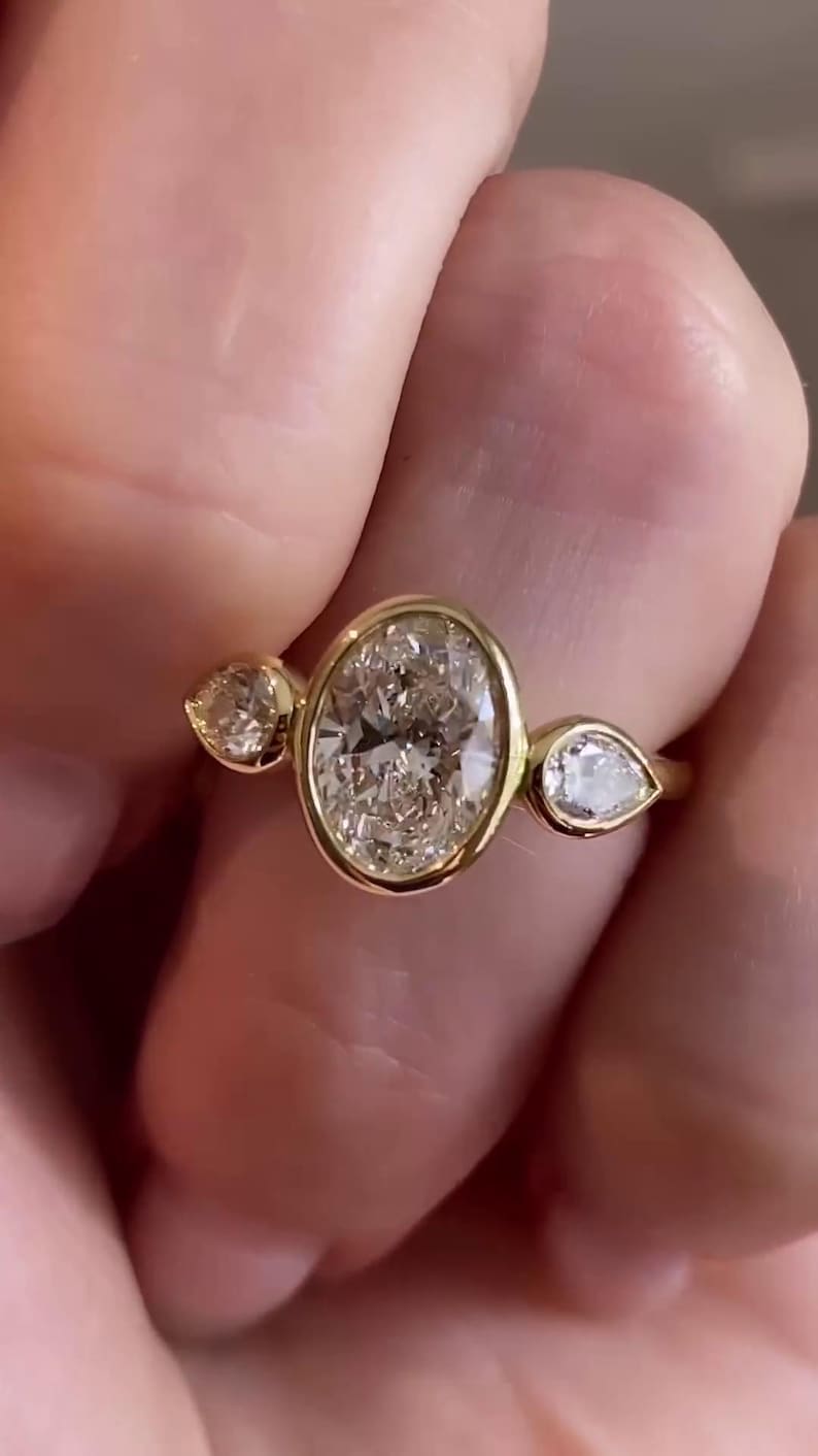 May include: A gold ring with a large oval-shaped diamond and two smaller pear-shaped diamonds on either side.