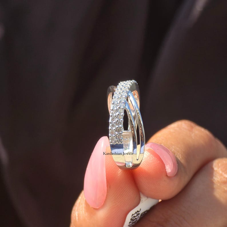 May include: A silver ring with a crossover design. One band is set with small, sparkling stones. The ring is held up against a dark background. The text "Kardashian Jewels" is visible on the ring.