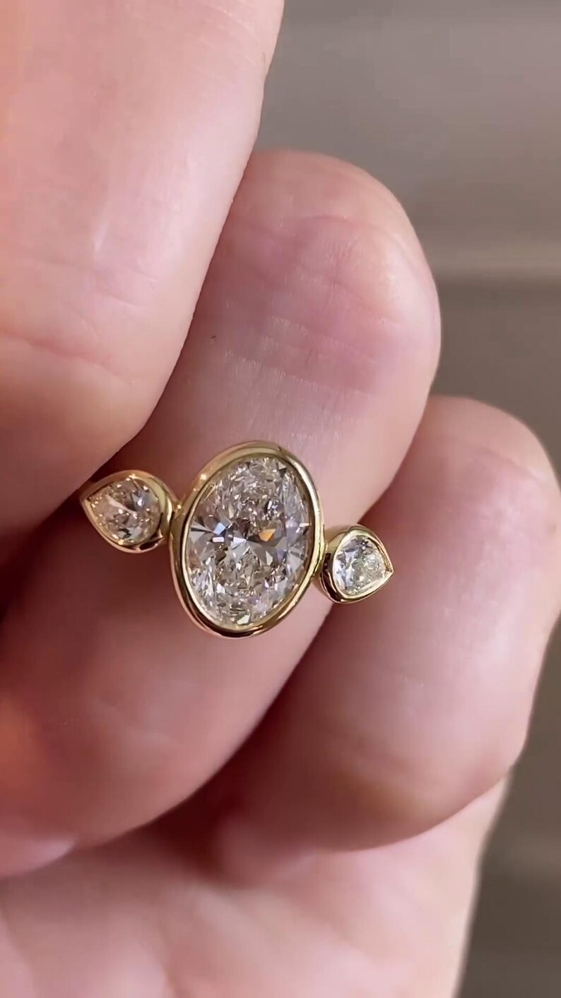 May include: A gold ring with a large oval-shaped diamond and two smaller pear-shaped diamonds on either side.