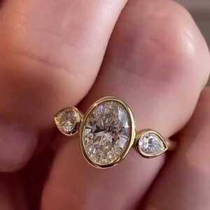 May include: A gold ring with a large oval-shaped diamond and two smaller pear-shaped diamonds on either side.