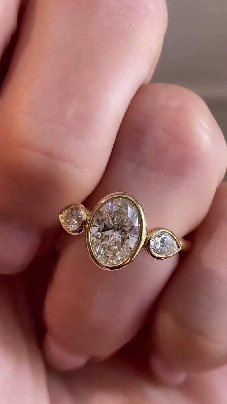 May include: A gold ring with a large oval-shaped diamond and two smaller pear-shaped diamonds on either side.