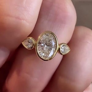 May include: A gold ring with three oval-shaped diamonds. The center diamond is larger than the two side diamonds.