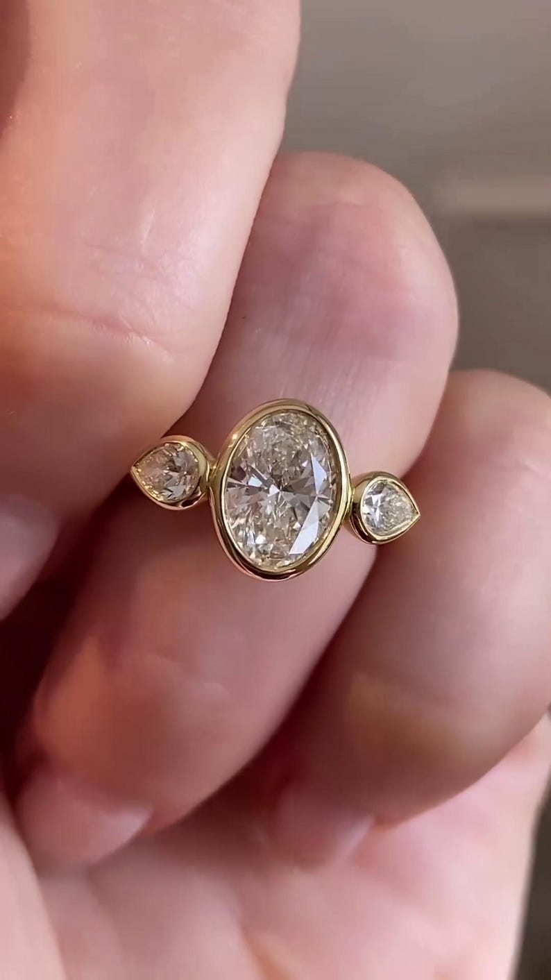 May include: A gold ring with three oval-shaped diamonds. The center diamond is larger than the two side diamonds.