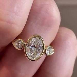 May include: A gold ring with three oval-shaped diamonds. The center diamond is larger than the two side diamonds.