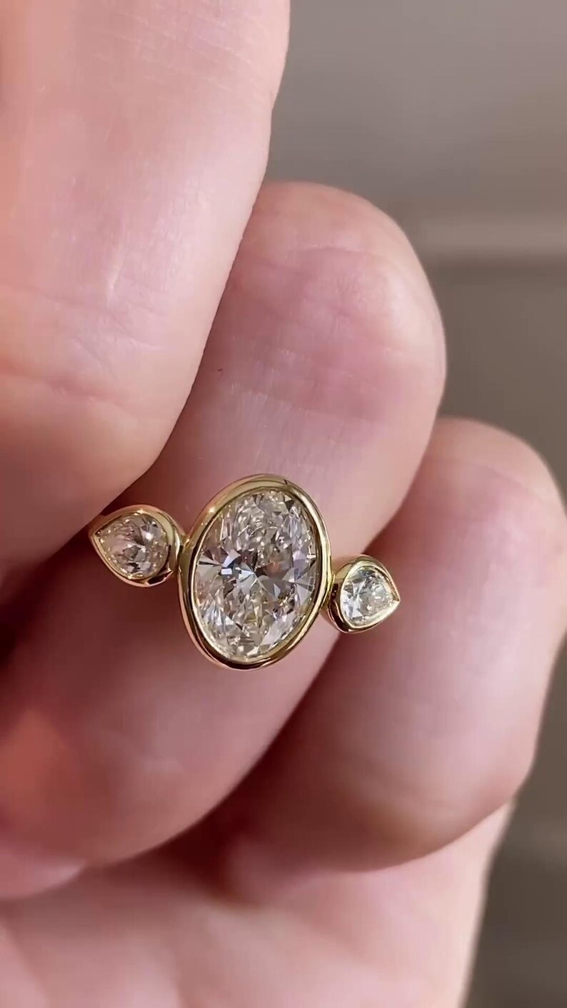 May include: A gold ring with three oval-shaped diamonds. The center diamond is larger than the two side diamonds.