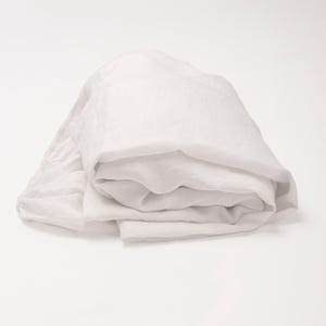 May include: A folded white linen sheet set. The bedding is neatly arranged, showcasing the soft texture and subtle folds of the fabric. The neutral color and simple design suggest a minimalist aesthetic.