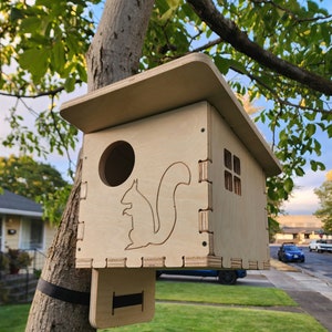 May include: A wooden squirrel house with a cutout of a squirrel on the front. The house is mounted on a tree trunk and has a small opening for the squirrel to enter.