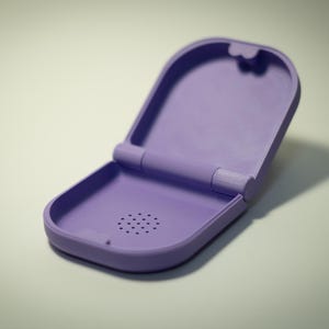 Puede incluir: Estuche lavanda abierto con tapa abisagrada. El estuche tiene forma rectangular redondeada con una serie de peque&ntilde;os agujeros cerca de la parte inferior. El estuche est&aacute; vac&iacute;o y se encuentra sobre una superficie clara.