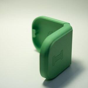 Puede incluir: Un estuche verde claro, abierto, de forma cuadrada con esquinas redondeadas. El estuche est&aacute; hecho de un material s&oacute;lido y tiene un peque&ntilde;o dise&ntilde;o en relieve en la parte delantera. El estuche est&aacute; abierto, revelando el interior.